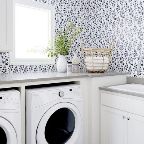 A white themed laundry room fitted with two white coloured front load washing machines and a dark blue coloured flower wallpaper finish on the wall