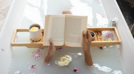 female reading book in milk bath strewn with flowers