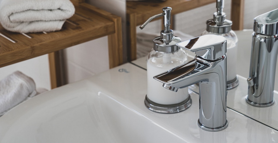 soap dispenser standing on white ceramic sink with stainless steel faucet